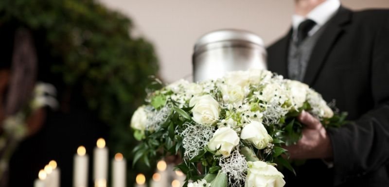 Urna z prochami wśród białych kwiatów i zniczy podczas pożegnania