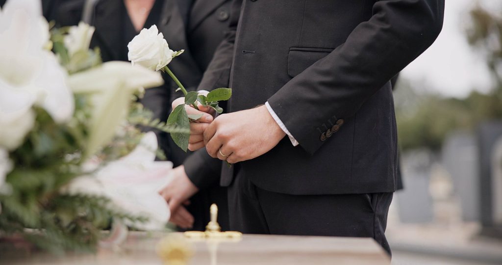 Uczestnik ceremonii pogrzebowej trzymający białą różę